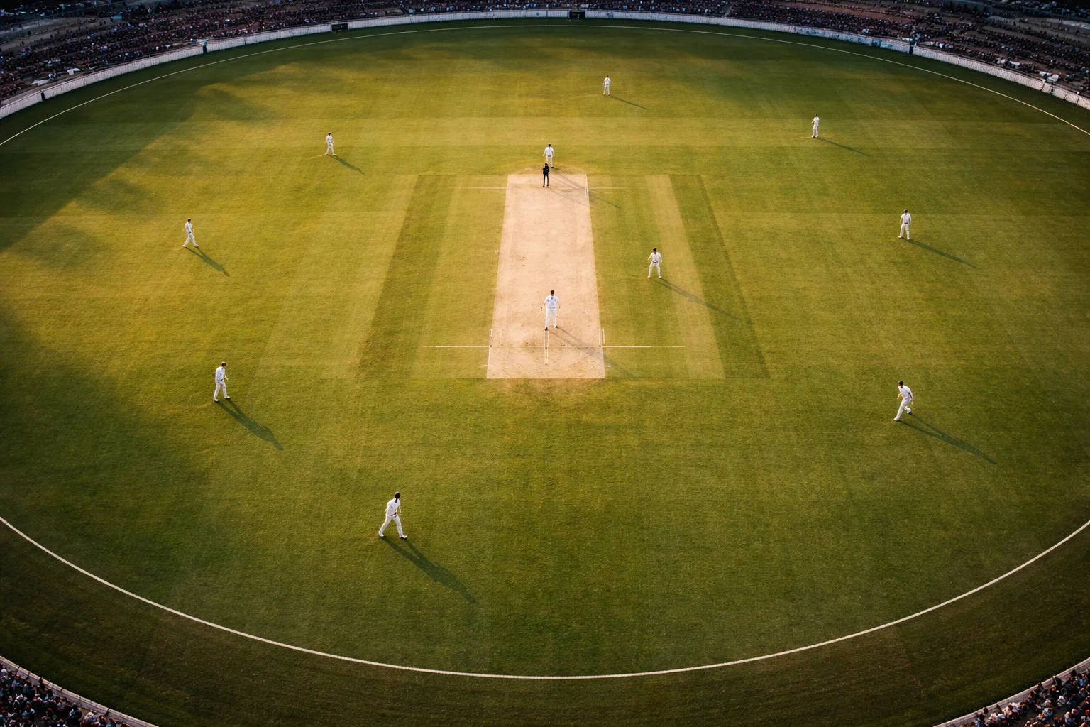 Campo di cricket visto dall'alto con pitch al centro e giocatori in posizione durante una partita internazionale